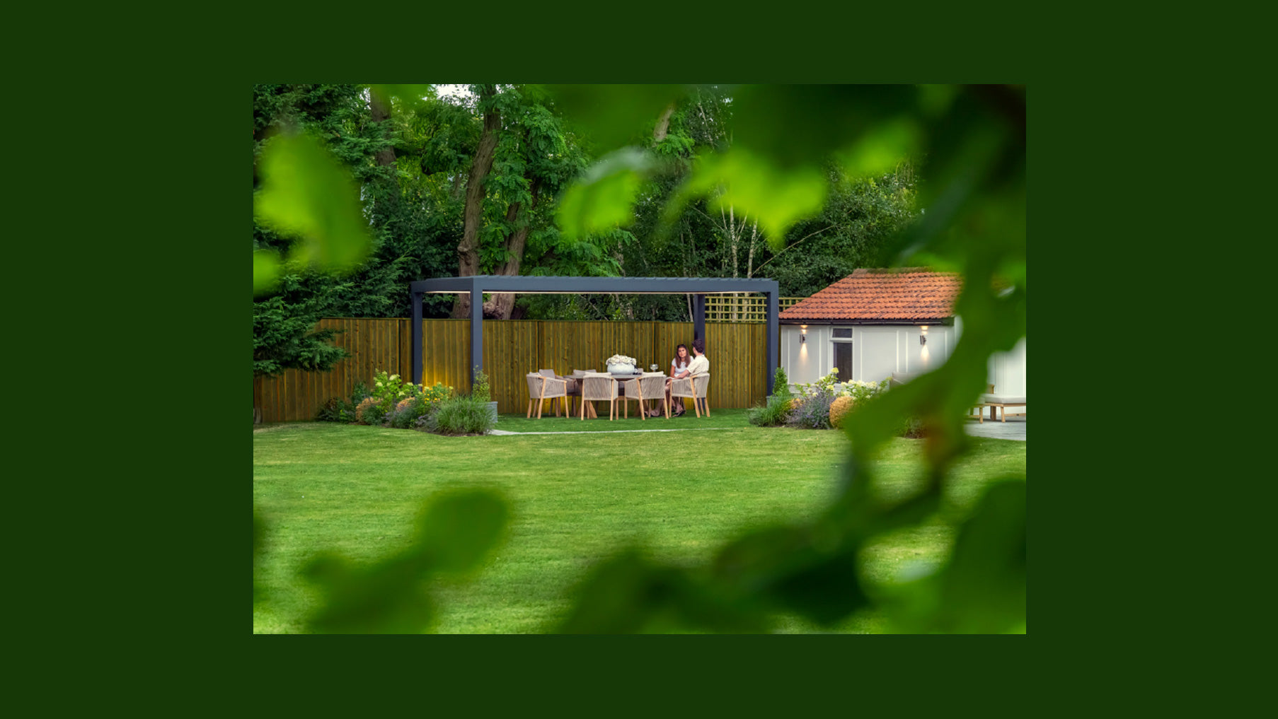 Backyard with outdoor furniture and a pergola, framed by green leaves.